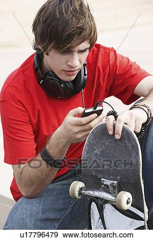 Stock Photo - Young skateboarder using MP3 Player outside. Fotosearch