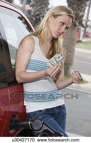 Stock Image - Young woman counting money at service station. Fotosearch