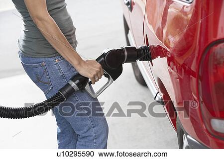 Stock Image - Young woman filling up car with gas, mid section. Fotosearch