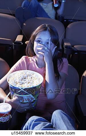 Young woman holding Popcorn, covering face with hand, watching movie in Theatre View Large Photo Image Stock Photo - Young woman holding Popcorn, covering face with hand, watching movie in Theatre. Fotosearch