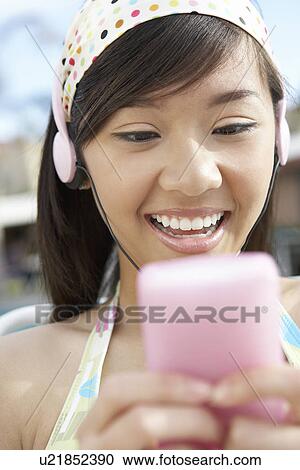Stock Image - Young woman listing to mp3 player, head and shoulders. Fotosearch