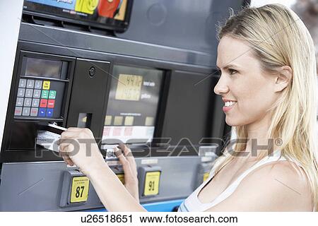 Stock Image - Young woman paying with credit card at gas pump, head and shoulders. Fotosearch