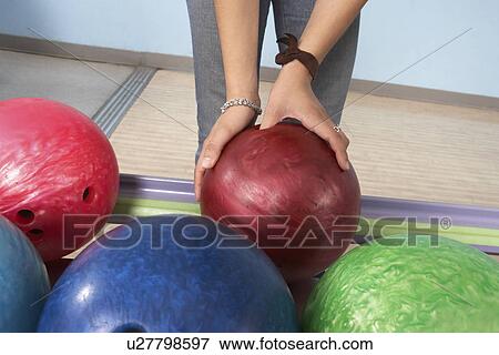 Stock Photo - Young woman selecting bowling ball, mid section. Fotosearch