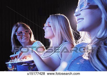 Stock Photo - Young woman sitting with Friends, Watching Movie in theatre. Fotosearch