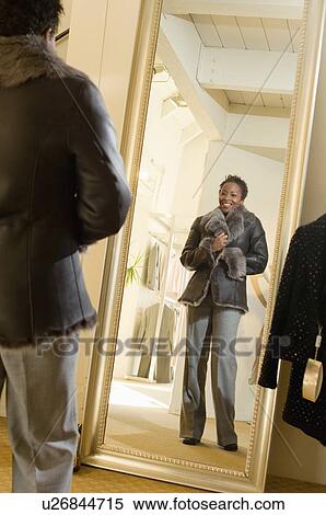 Young woman trying on coat in front of mirror, portrait View Large Photo Image Stock Photography - Young woman trying on coat in front of mirror, portrait. Fotosearch