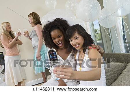 Stock Image - Young women photographing themselves using mobile phone at bridal shower. Fotosearch