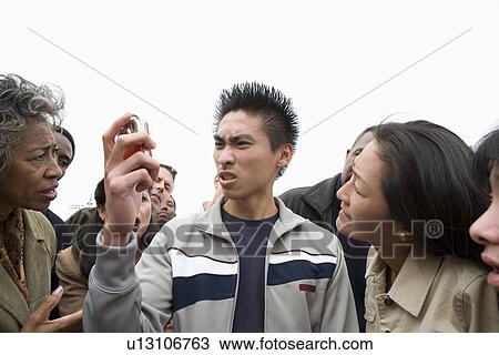 Angry young man holding mobile phone in crowd View Large Photo Image Stock Image - Angry young man holding mobile phone in crowd. Fotosearch