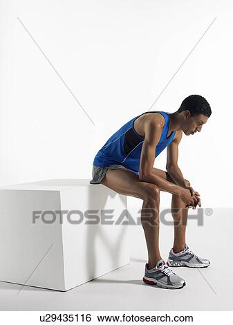 Stock Photograph - Athlete sitting on box, side view. Fotosearch