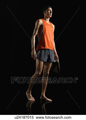 Stock Photography - Athlete standing, holding shoes, low angle view. Fotosearch