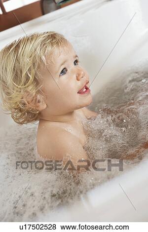 Stock Photo - Baby Boy sitting in a bubble-filled Bathtub, side view. Fotosearch