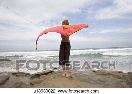 Stock Image - Back view of boy standing on beach and watching sea. Fotosearch