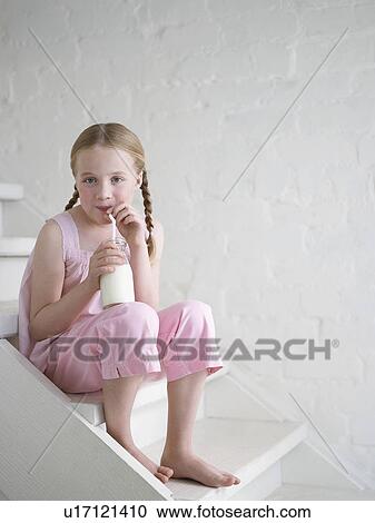 Stock Image - Barefoot Girl Drinking Glass of Milk, sitting on stairs. Fotosearch