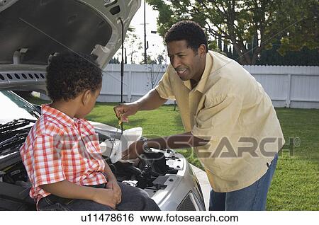 Stock Photograph - Boy (5-6) assisting father checking oil level in car. Fotosearch