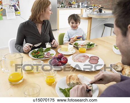 Stock Photography - Boy (5-6) eating lunch with parents at dining room table. Fotosearch