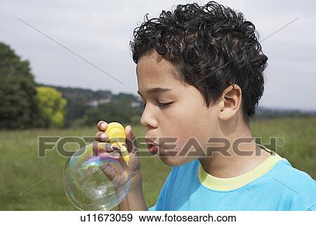 Boy (7-9) blowing bubbles in field View Large Photo Image Stock Photo - Boy (7-9) blowing bubbles in field. Fotosearch