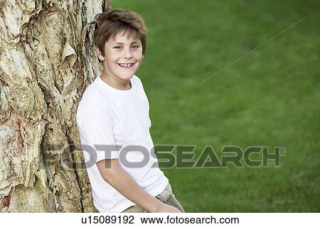 Boy leaning against tree, portrait View Large Photo Image Stock Image - Boy leaning against tree, portrait. Fotosearch