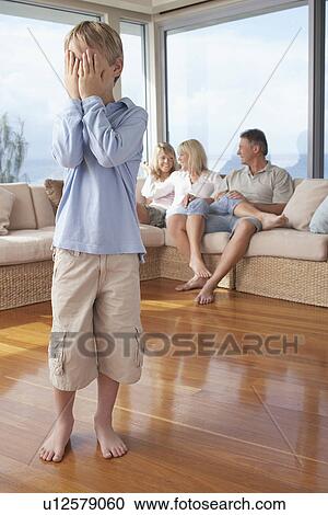Stock Image - Boy standing, Hiding Face from Family in Background. Fotosearch