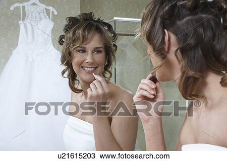 Stock Image - Bride applying lipstick in mirror. Fotosearch