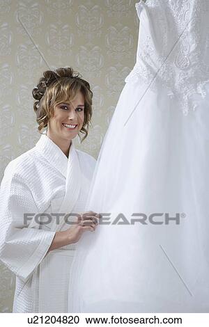 Bride in bathrobe touching wedding dress View Large Photo Image Stock Image - Bride in bathrobe touching wedding dress. Fotosearch