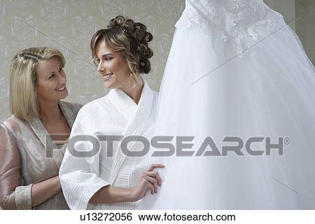 Bride in bathrobe touching wedding dress, mother looking on View Large Photo Image Stock Photograph - Bride in bathrobe touching wedding dress, mother looking on. Fotosearch
