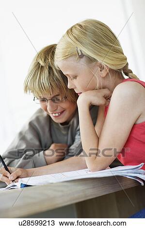 Stock Image - Brother and Sister Doing Homework at table in home. Fotosearch
