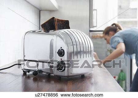 Stock Photograph - Burned toast in toaster, woman in background. Fotosearch