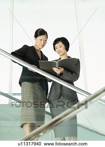 Stock Image - Business colleagues reviewing documents while standing on stairs. Fotosearch