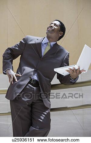 Business man holding laptop, looking up View Large Photo Image Stock Image - Business man holding laptop, looking up. Fotosearch