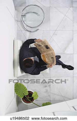 Stock Image - Business man reading newspaper in lobby, view from above. Fotosearch