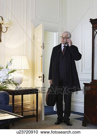 Stock Image - Business man standing in room using mobile phone. Fotosearch