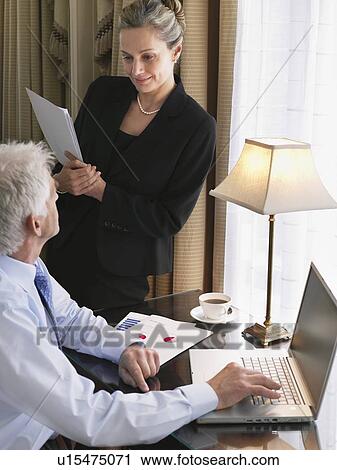Business man using laptop, business woman sitting on desk reading documents, elevated view View Large Photo Image Stock Image - Business man using laptop, business woman sitting on desk reading documents, elevated view. Fotosearch