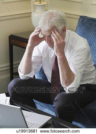 Stock Image - Business man using laptop sitting on sofa, elevated view. Fotosearch