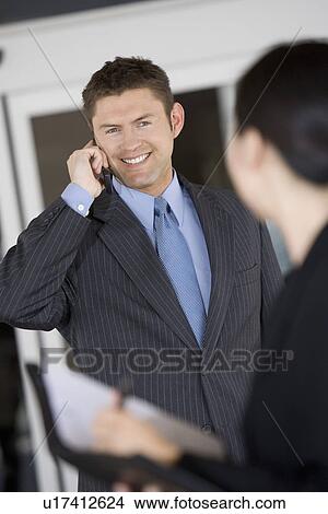 Business man using mobile phone with colleague in office View Large Photo Image Picture - Business man using mobile phone with colleague in office. Fotosearch
