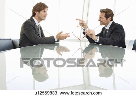 Stock Image - Business men talking at conference table. Fotosearch