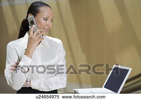 Stock Photography - Business woman using mobile phone and laptop in office. Fotosearch