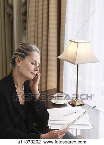 Stock Image - Business woman using mobile phone sitting at desk, elevated view. Fotosearch