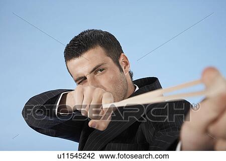 Businessman aiming rubber band, on blue background View Large Photo Image Stock Image - Businessman aiming rubber band, on blue background. Fotosearch