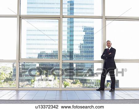 Stock Image - Businessman by window in office building, portrait. Fotosearch
