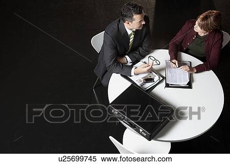 Stock Photography - Businessman conferring with woman at round table, elevated view. Fotosearch