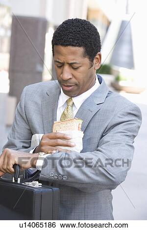 Businessman eating sandwich and checking time View Large Photo Image Stock Photograph - Businessman eating sandwich and checking time. Fotosearch