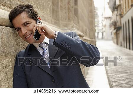 Stock Photography - Businessman leaning on building in street, using mobile phone.. Fotosearch