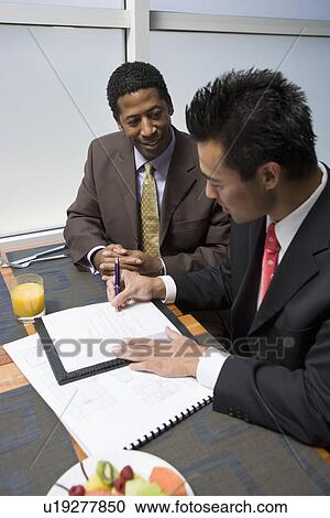Businessman looking while another businessman signs agreement View Large Photo Image Stock Image - Businessman looking while another businessman signs agreement. Fotosearch