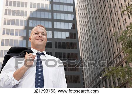 Stock Image - Businessman outside office building, smiling. Fotosearch