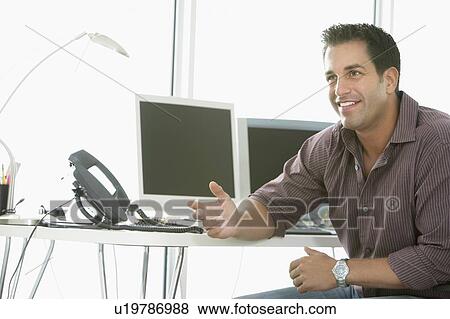 Stock Photo - Businessman smiling by computers in office. Fotosearch