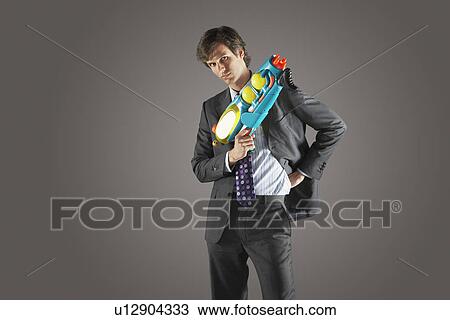 Stock Image - Businessman standing, holding water gun, hand on hip. Fotosearch