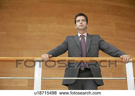 Businessman standing in office, holding railing, low angle view. View Large Photo Image Stock Photo - Businessman standing in office, holding railing, low angle view.. Fotosearch