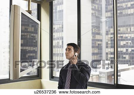 Businessman using cell phone looking at flat screen TV in office, half length View Large Photo Image Stock Photograph - Businessman using cell phone looking at flat screen TV in office, half length. Fotosearch
