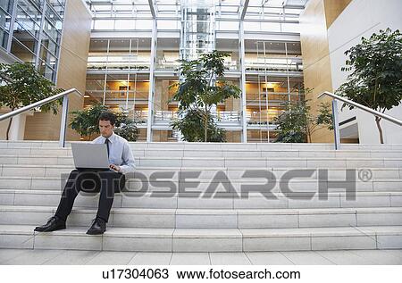 Stock Image - Businessman using laptop on steps outside office. Fotosearch