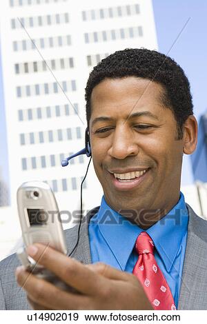 Stock Photo - Businessman using mobile, outdoors, smiling. Fotosearch