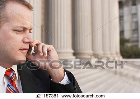 Stock Image - Businessman using mobile phone outside courthouse. Fotosearch